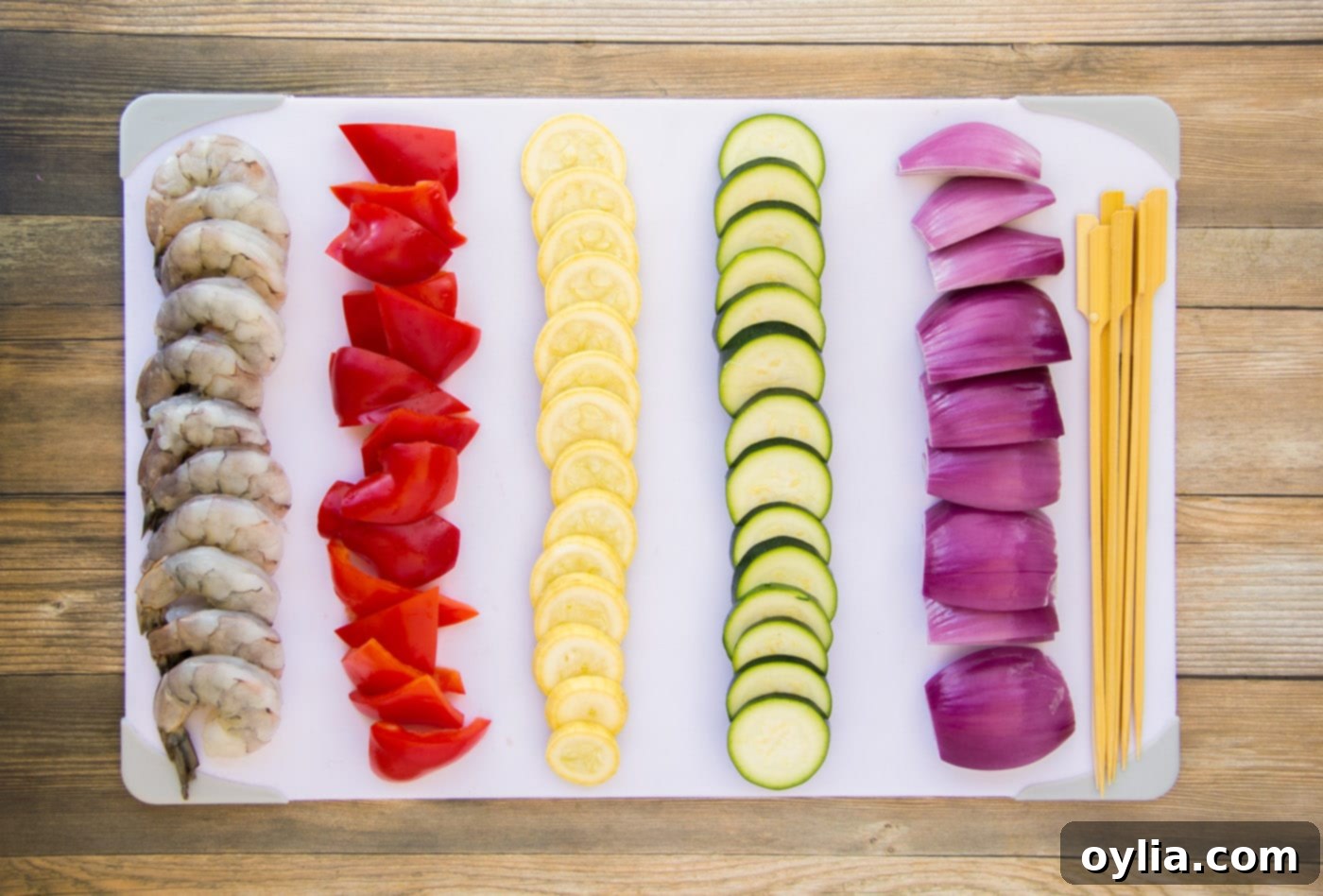 Assorted sliced vegetables including bell peppers, squash, and red onion, ready for skewers.