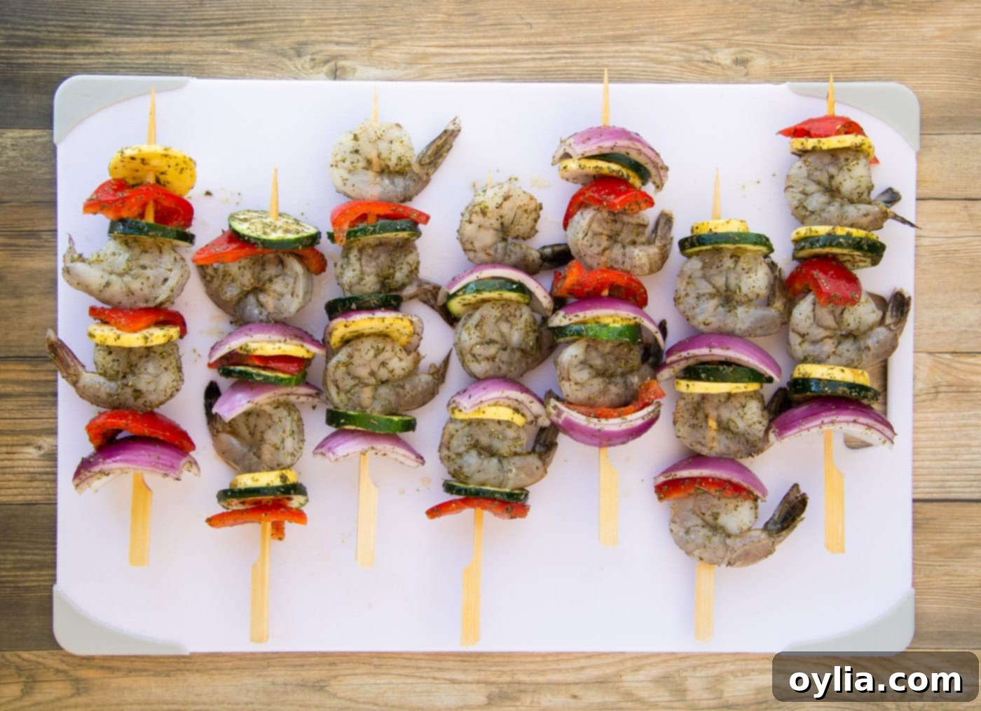 Assembled shrimp kabobs with fresh veggies on a cutting board, ready for grilling.