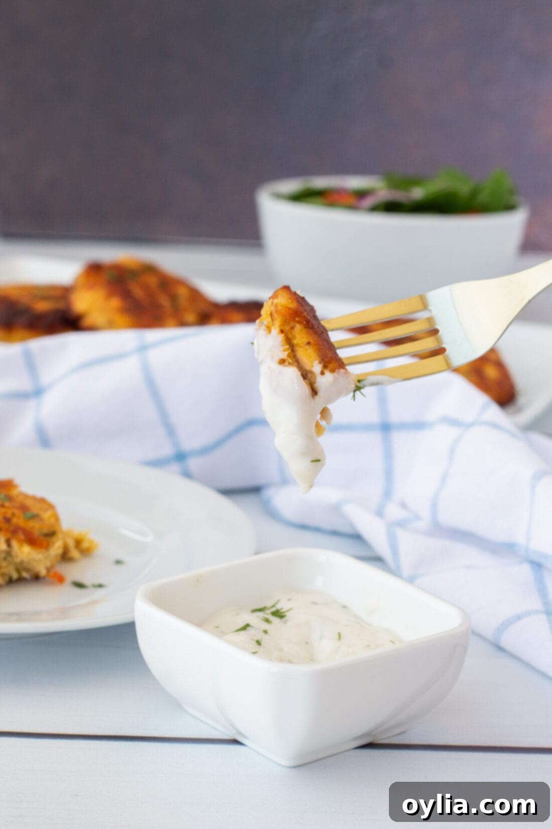 A fork holding a piece of smoked salmon fish cake, dipped in a creamy white sauce.