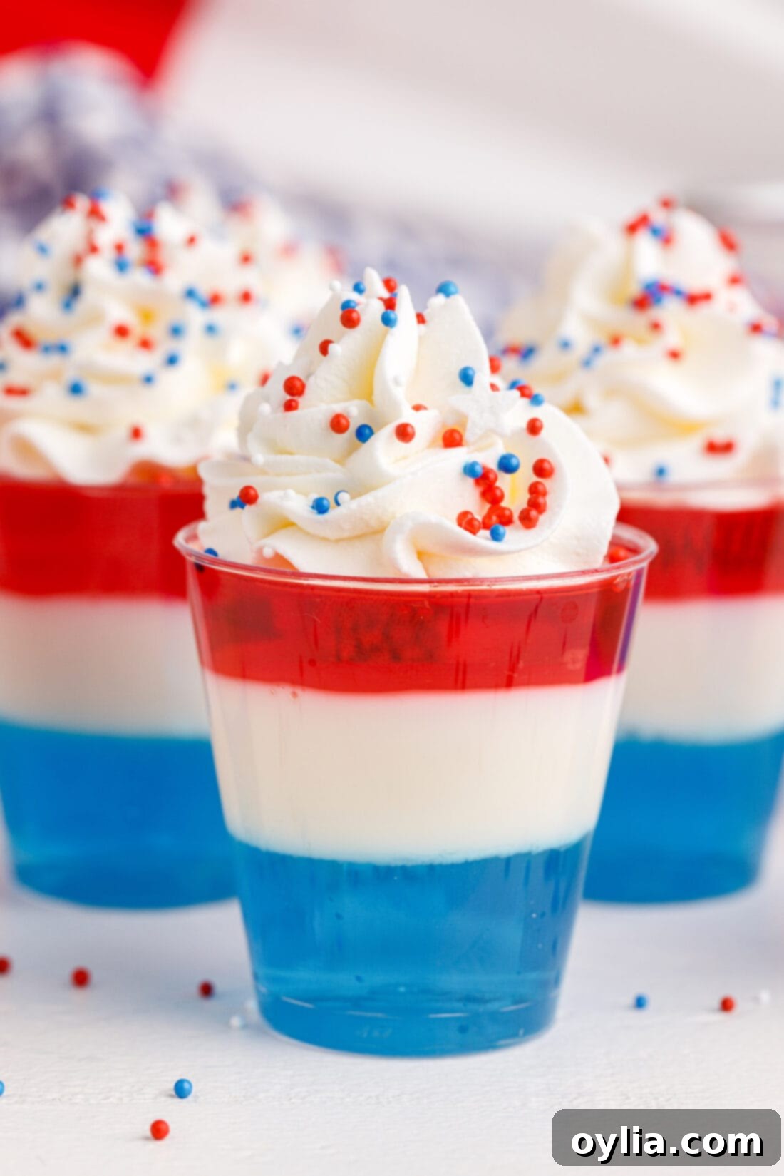 Colorful 4th of July Jello Shots topped with whipped cream and patriotic sprinkles, ready for a celebration