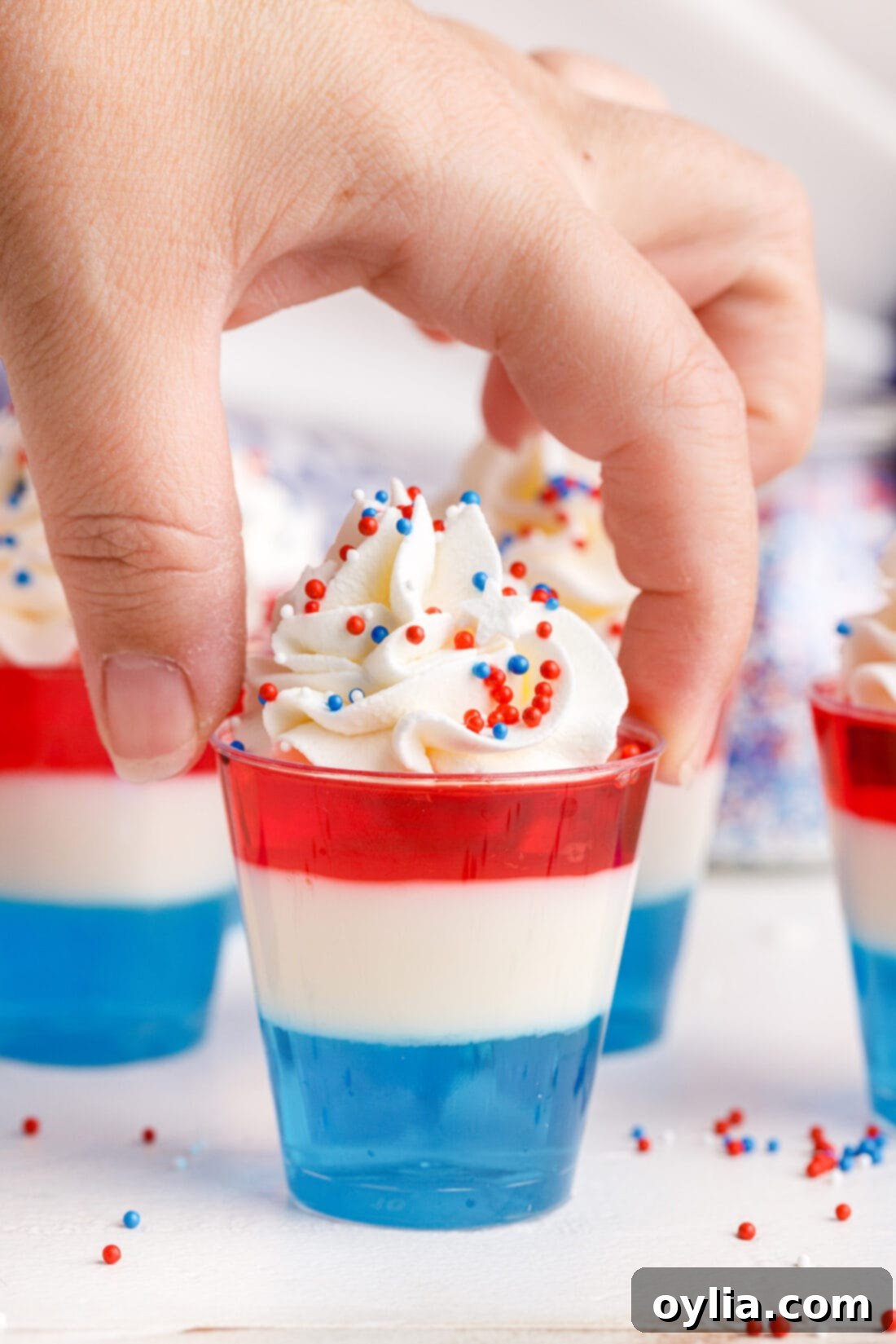 Hand picking up a vibrant red, white, and blue 4th of July Jello Shot from a tray