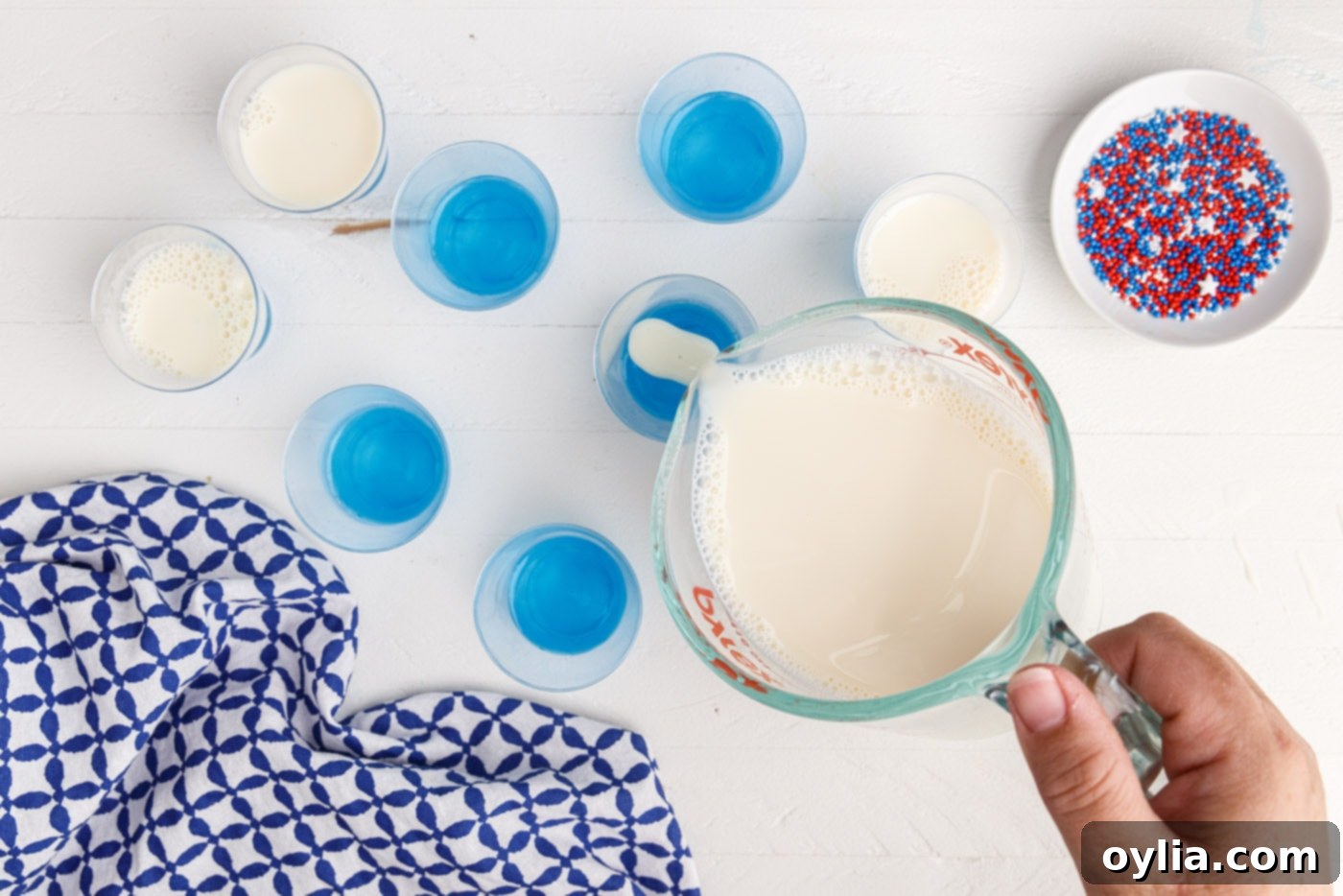 Pouring the white sweetened condensed milk jello layer over the set blue layer in shot glasses