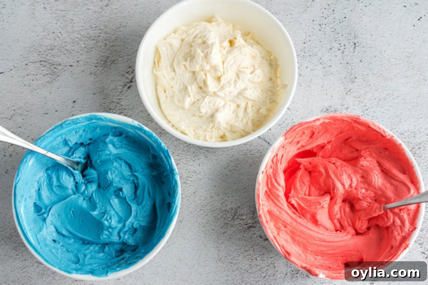 red, white, and blue buttercream frosting in separate bowls