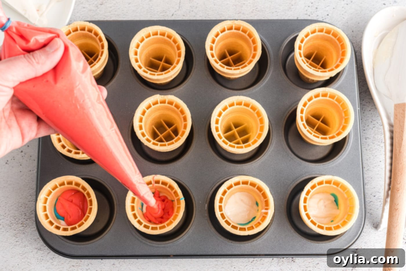 piping red cake batter inside an ice cream cone as the second layer