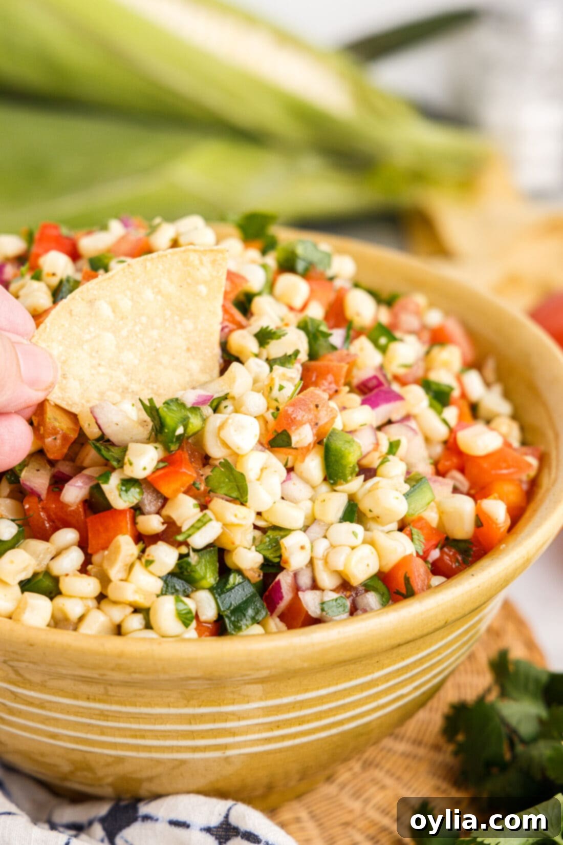 A tortilla chip being dipped into a bowl of vibrant, fresh corn salsa, showcasing its colorful ingredients like corn, tomatoes, and bell peppers.
