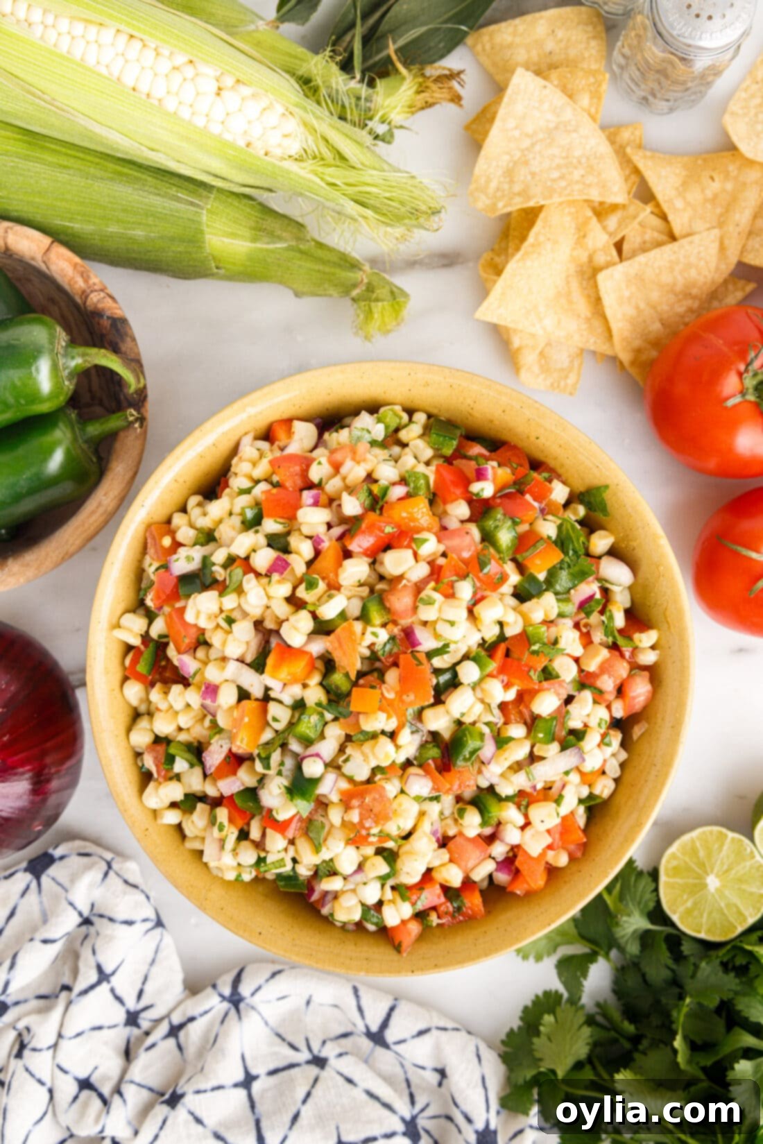 A close-up shot of a large white bowl filled with homemade corn salsa, showing the vibrant mixture of yellow corn, red tomatoes, green cilantro, and red bell peppers.