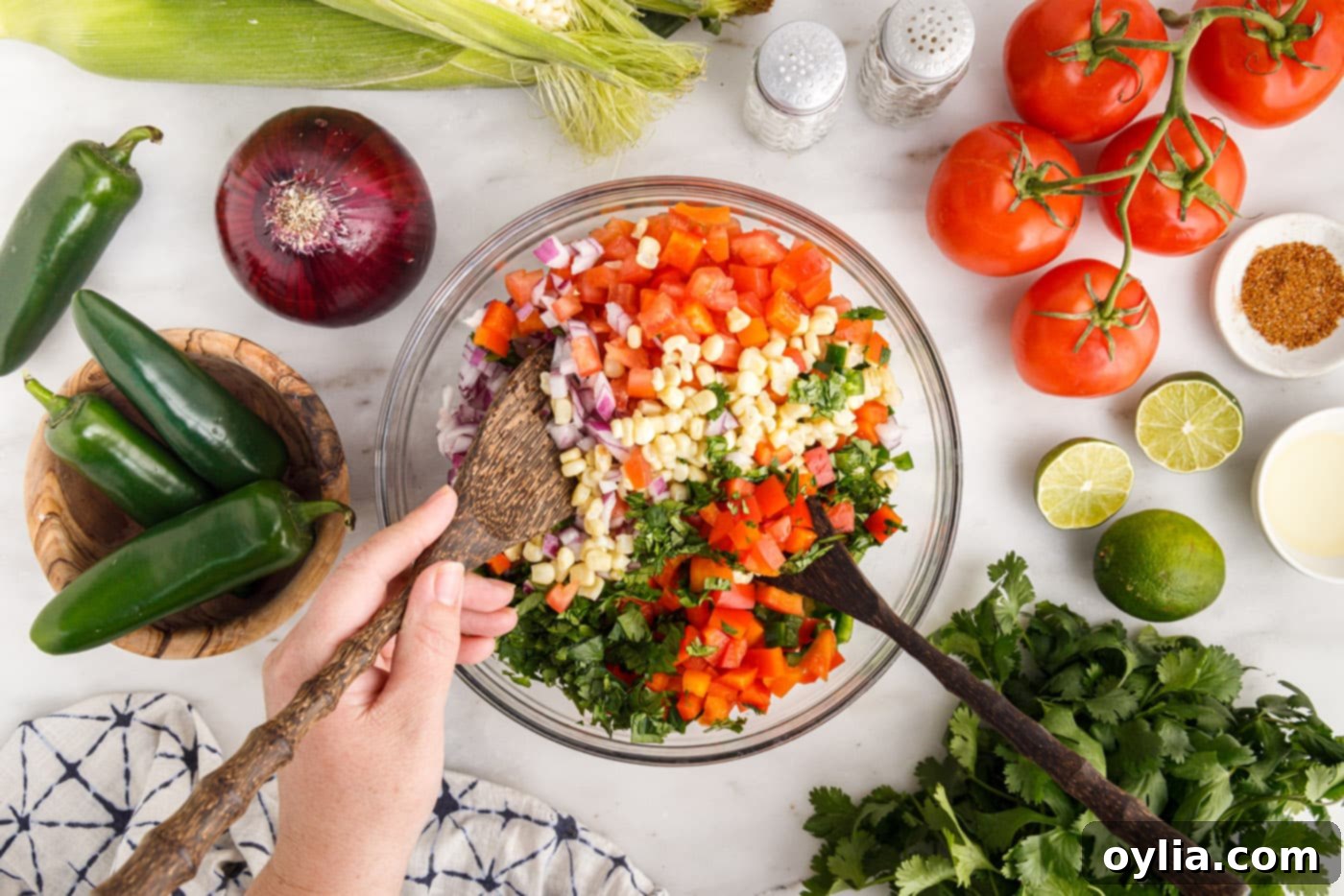 Mixing corn, tomatoes, onion, cilantro, and bell peppers together in a bowl before adding the dressing.