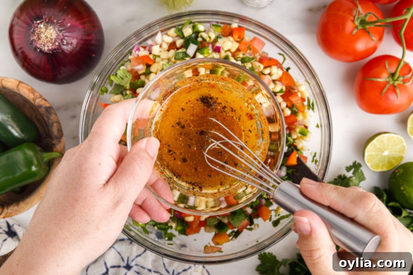 Pouring a vibrant chili-lime seasoning dressing over the mixed corn salsa ingredients in a bowl.