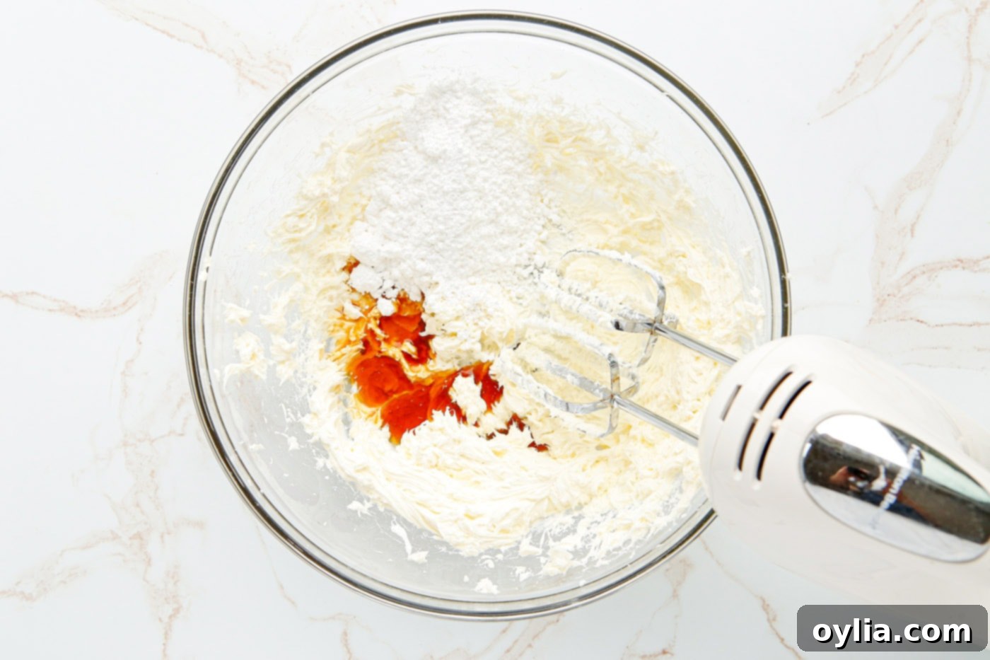 Powdered sugar, heavy cream, and vanilla being added to the cream cheese mixture.