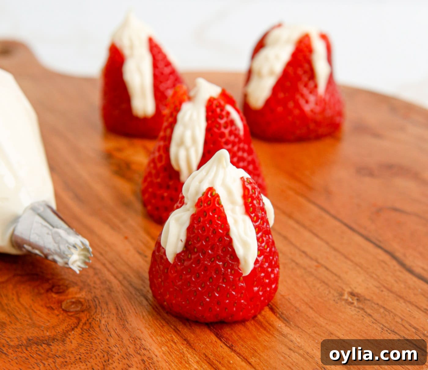Piping cheesecake filling into prepared strawberries.