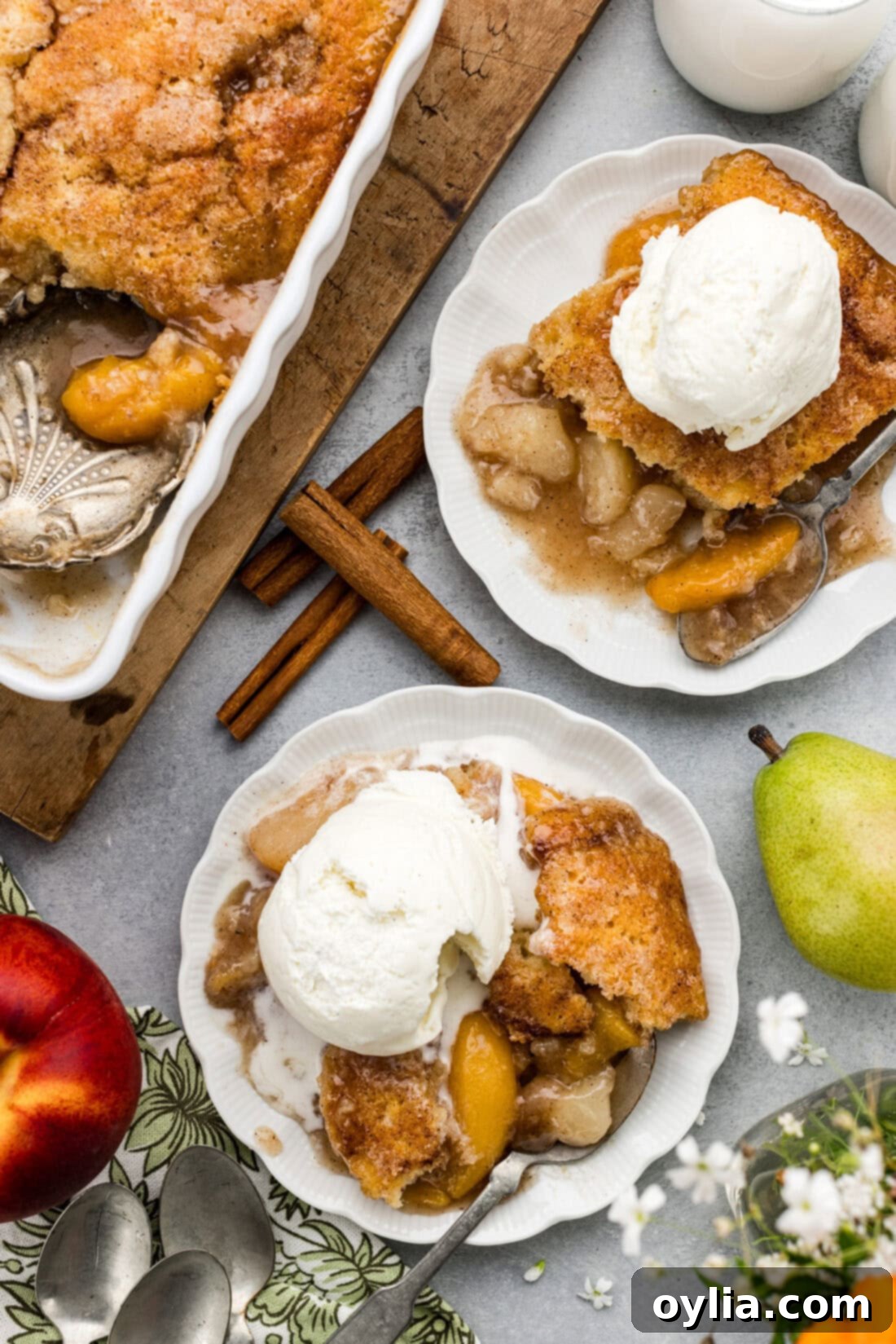 Two plates of Pear-Peach Cobbler, each generously topped with a scoop of vanilla ice cream, presented on a rustic wooden surface.