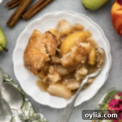 Close up photo of a plate of Pear-Peach Cobbler topped with a scoop of ice cream, showing the rich fruit and golden crust.