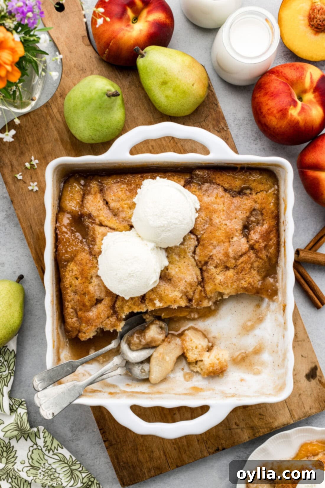A large baking dish of Pear-Peach Cobbler, freshly baked and topped with two melting scoops of vanilla ice cream, ready to be served.