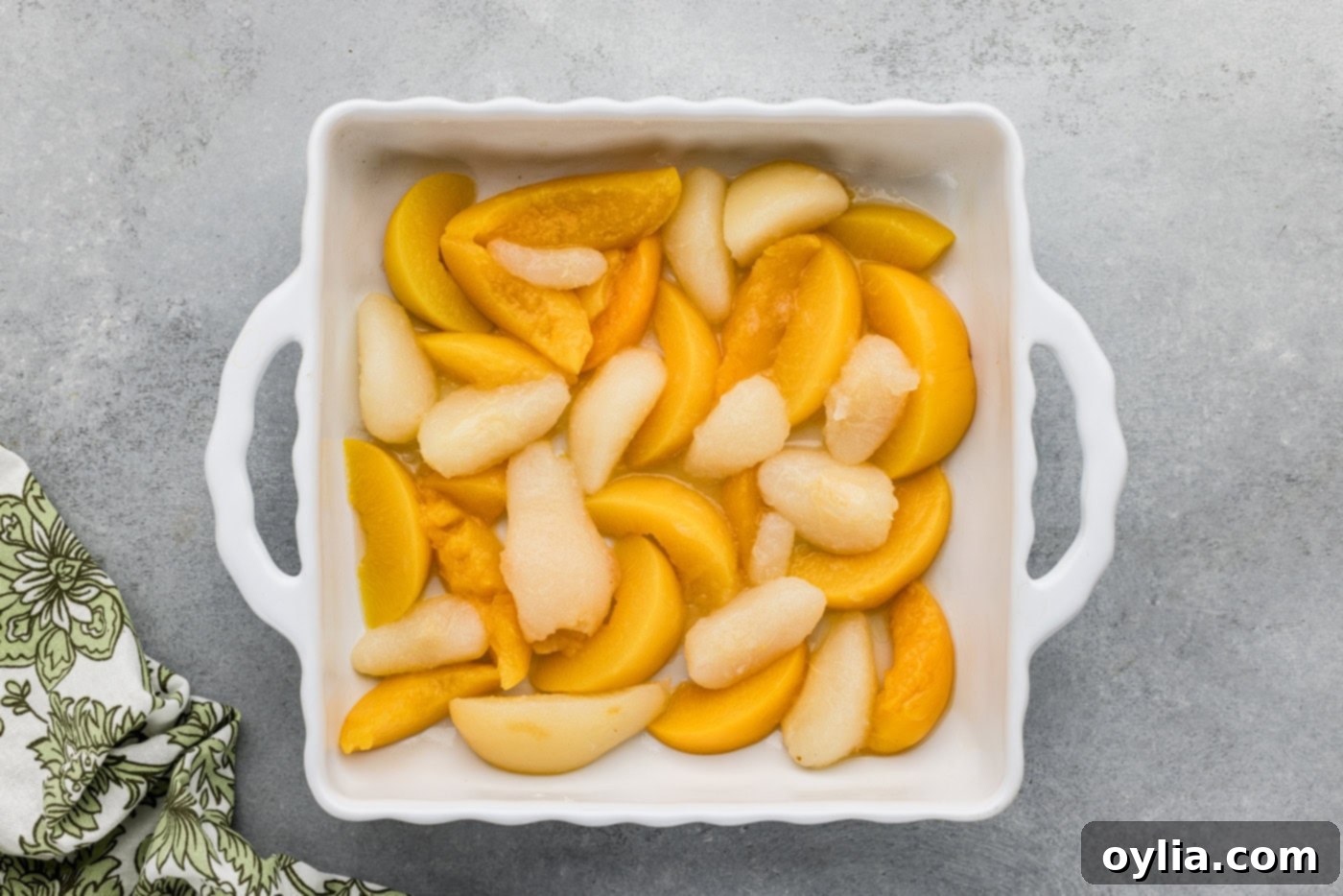 Drained canned peaches and pears spread in a single layer at the bottom of a prepared 9x9 inch baking dish.