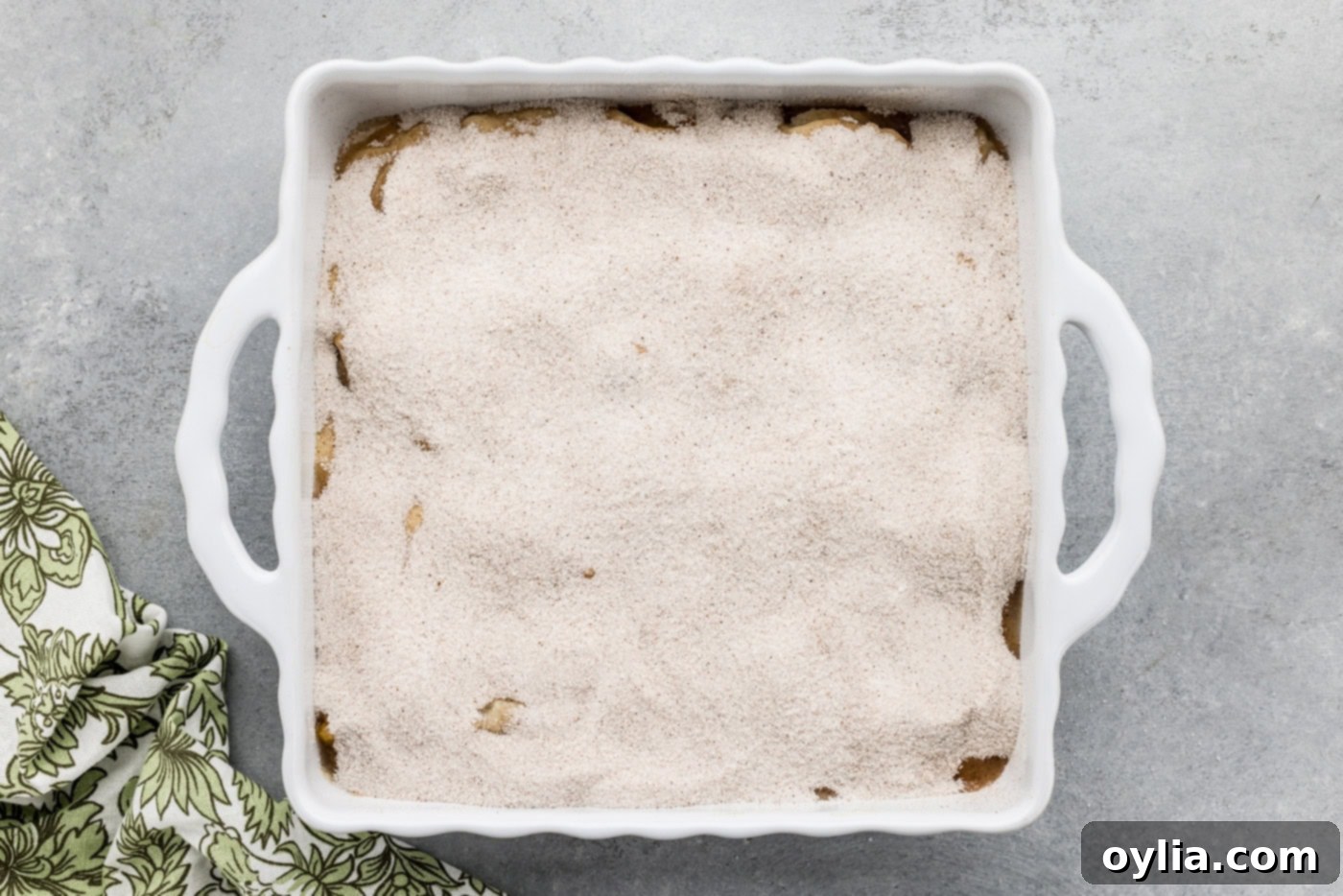 An overhead view of the baking dish, showing the cobbler batter fully covered with an even layer of spiced sugar mixture.