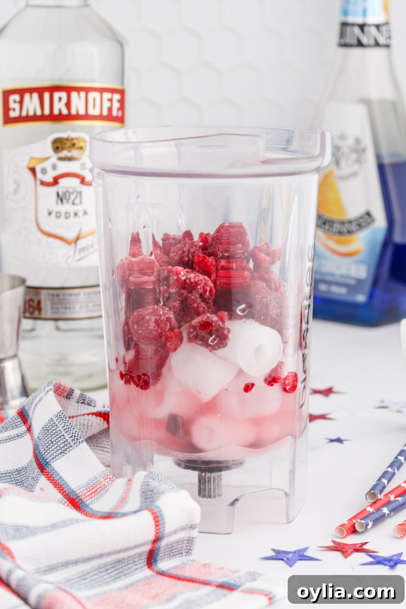 Raspberry, lemonade, ice, and vodka in a blender being prepared for the red layer