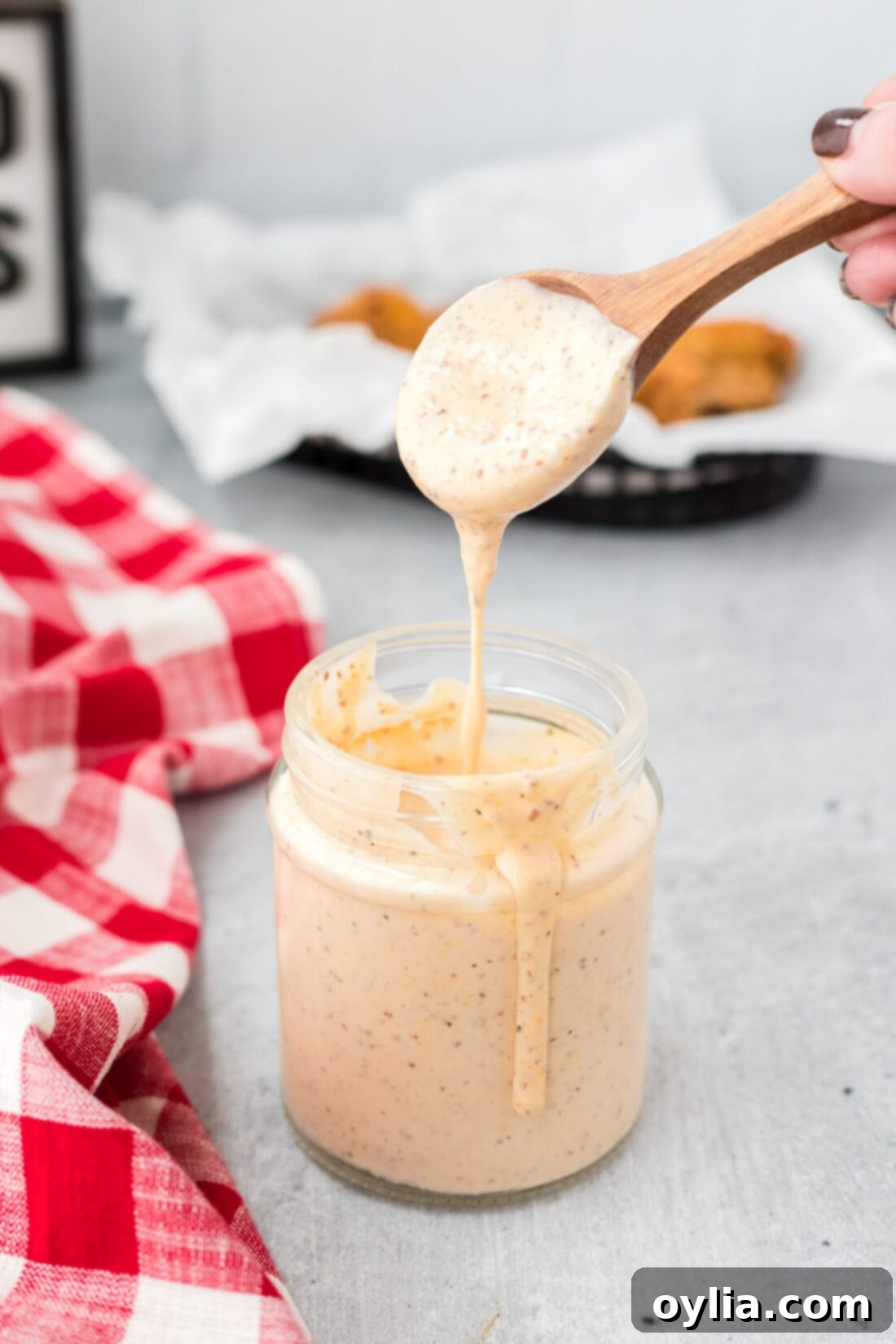 Spoon dripping creamy homemade Alabama White Sauce into a glass mason jar, showcasing its smooth texture