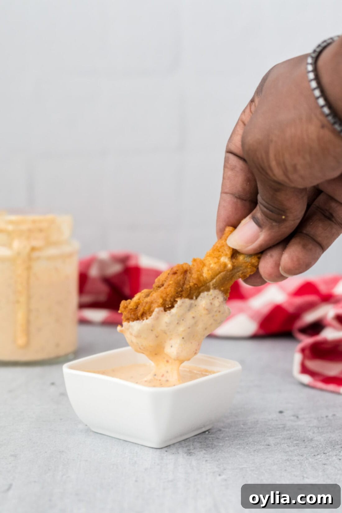 Crispy baked chicken wing being dipped into a bowl of creamy Alabama White Sauce, highlighting its use as a versatile dip