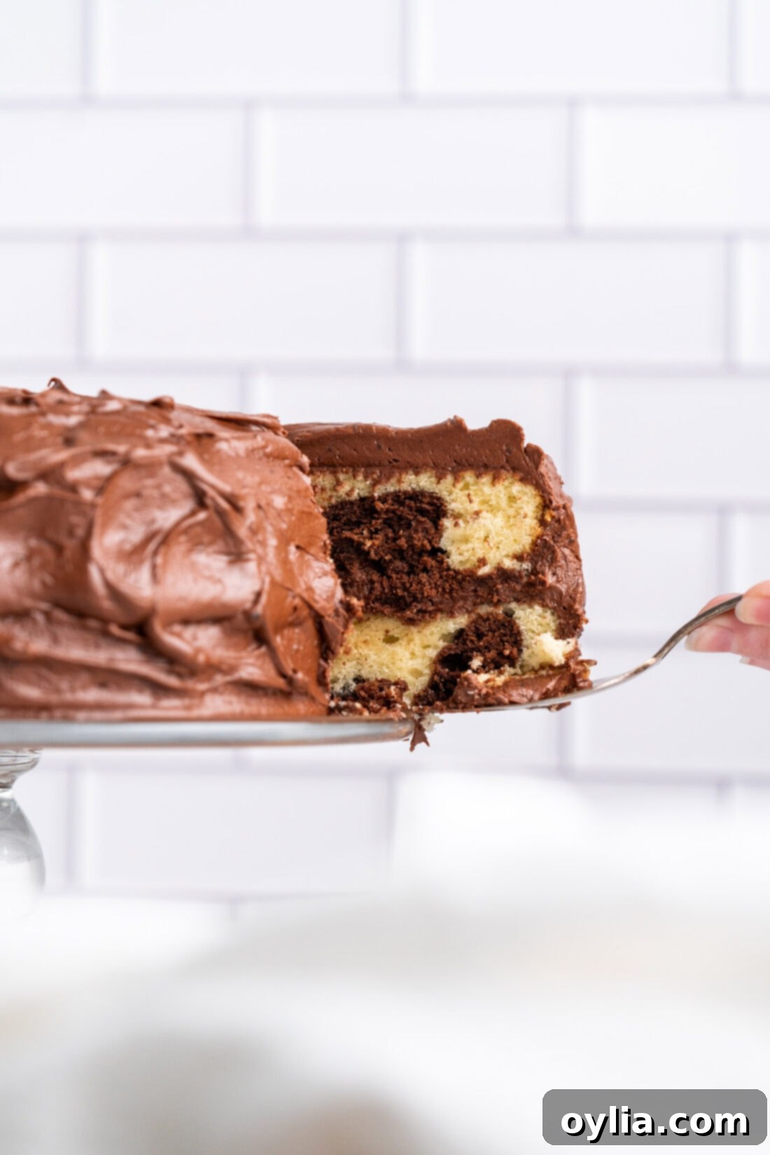 slice of Marble Cake on spatula, showcasing the beautiful chocolate and vanilla swirls and thick fudge frosting