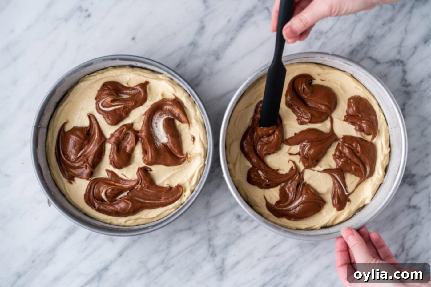 A spatula gently swirling chocolate batter into yellow batter in a round cake pan