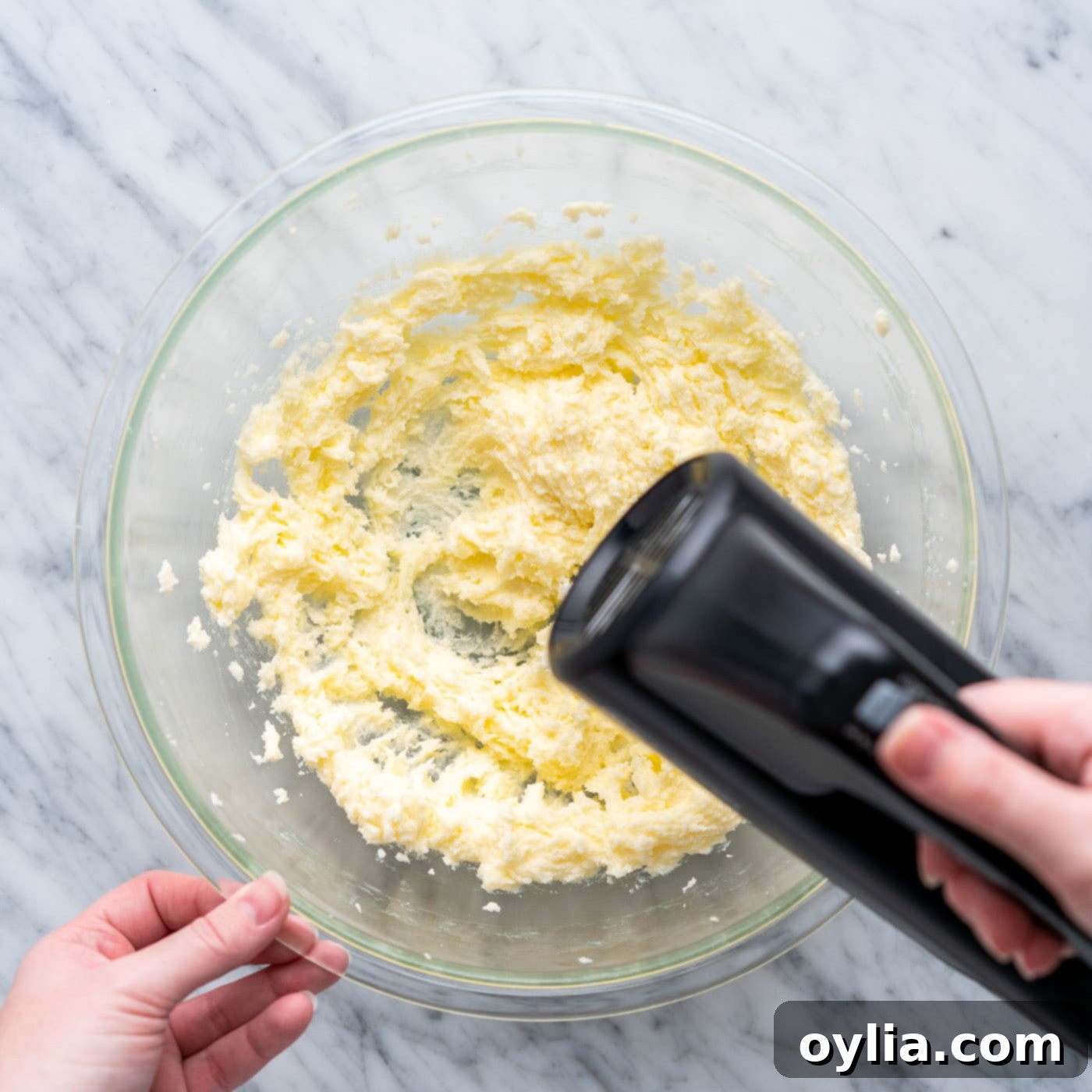 Butter and granulated sugar being creamed together in a large bowl with a handheld electric mixer