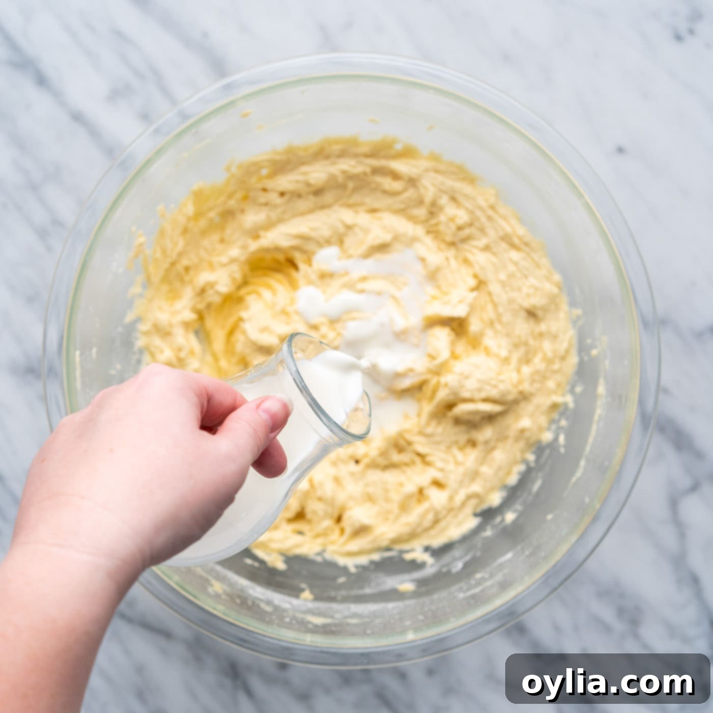 Milk being poured into yellow cake batter during the mixing process