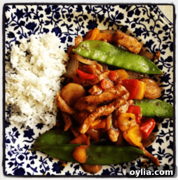 An overhead photo of a plate of peppered pork stir fry with sweet peppers with rice on the side.