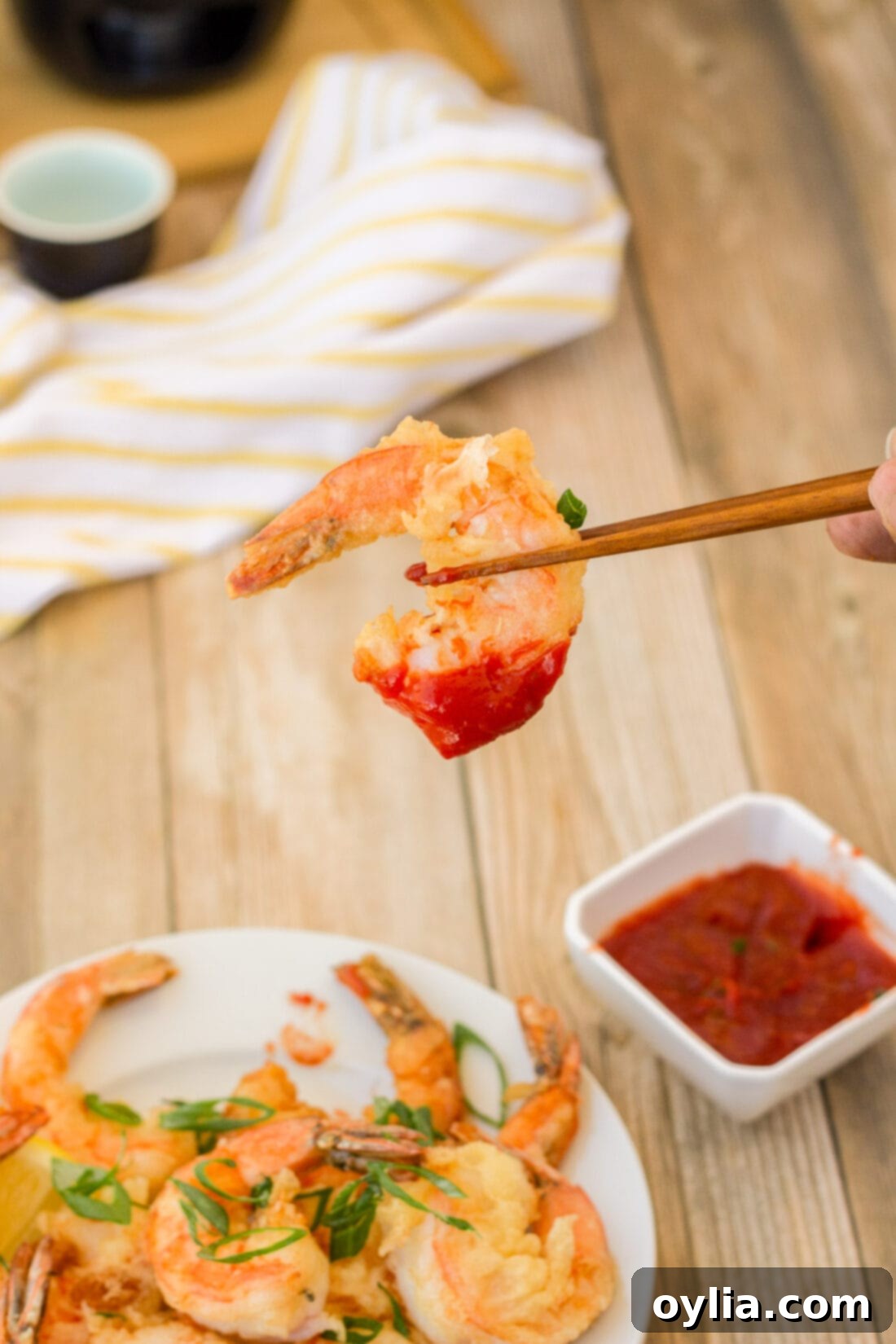 A hand holding a single piece of crispy pan-fried shrimp with chopsticks, ready to eat.