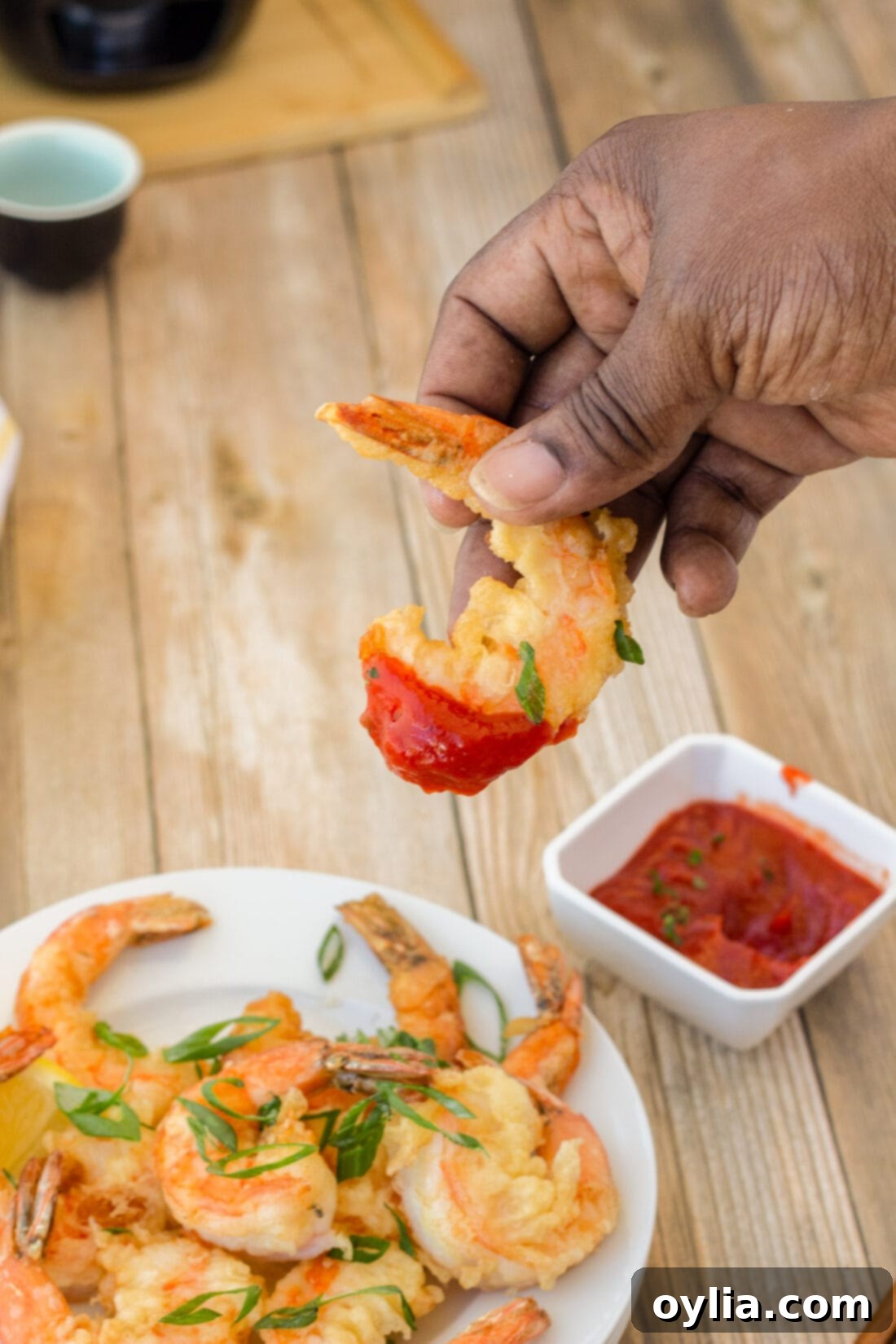 A close-up of crispy shrimp being dipped into a rich cocktail sauce, highlighting its golden texture.
