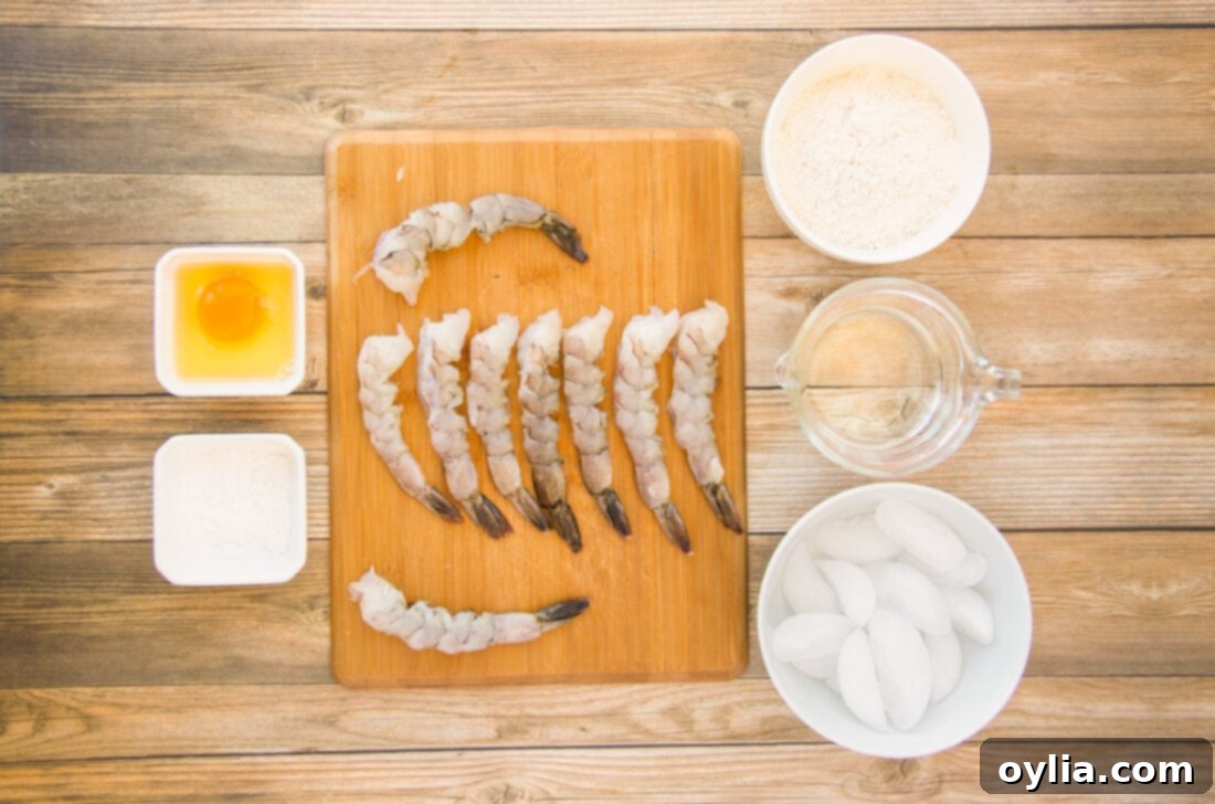 A flat lay of all the fresh ingredients required for making crispy shrimp: raw shrimp, cornstarch, egg, flour, and iced water.