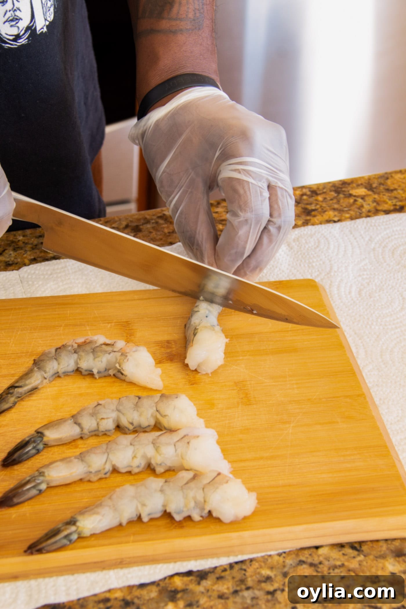 Scoring the underside of a raw shrimp with a knife to prevent curling during frying.