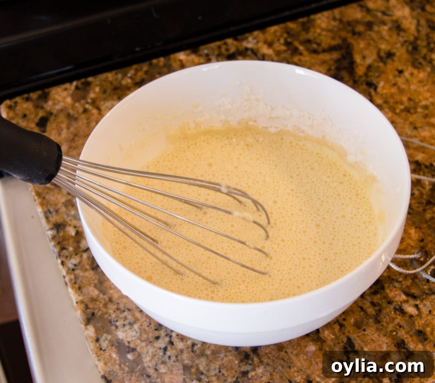 A bowl showing whisked egg, flour, and iced water, forming a smooth batter for the shrimp.