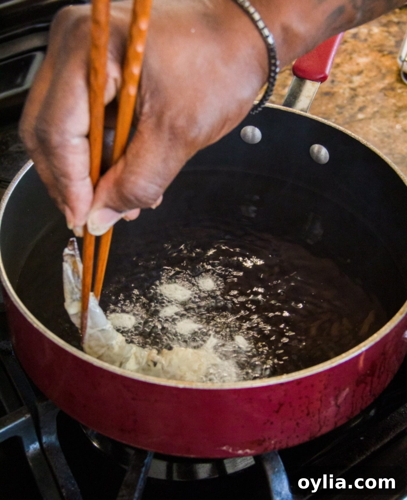 Carefully placing a battered shrimp into hot oil in a skillet using tongs.