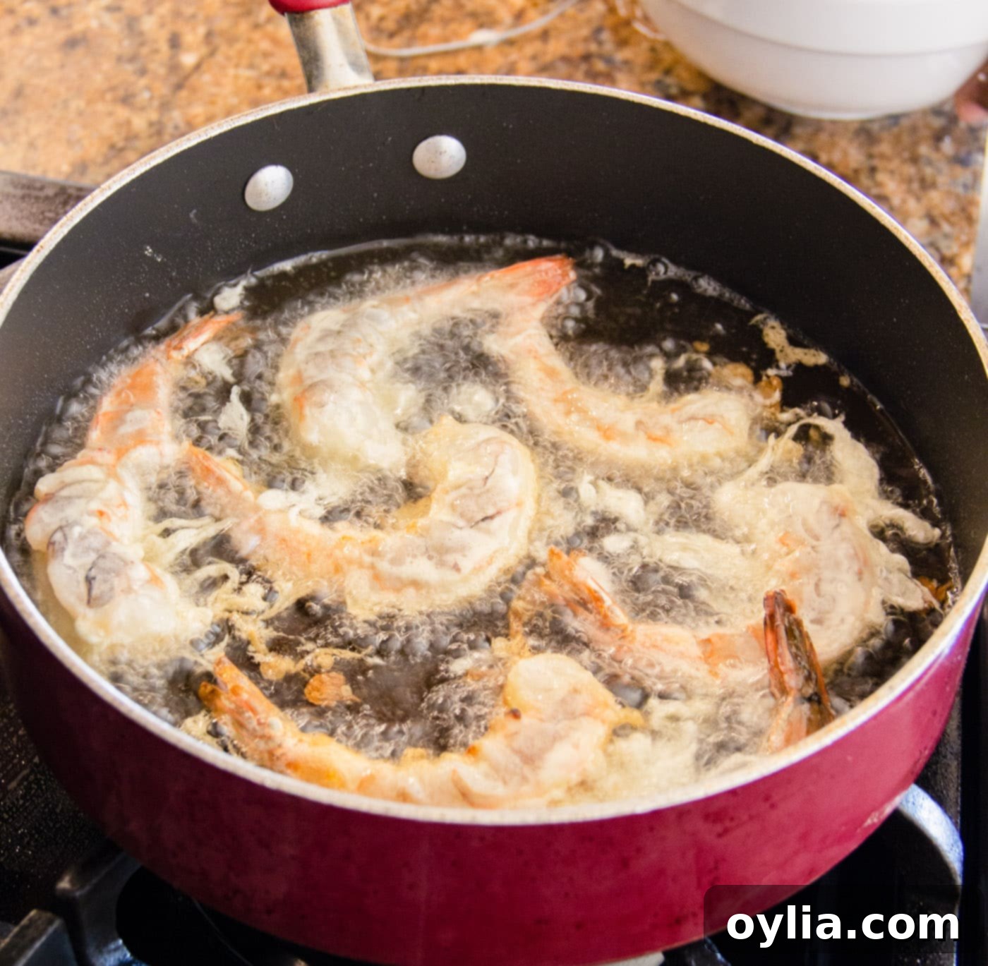 Several crispy shrimp frying in hot oil in a cast iron skillet, turning golden brown.