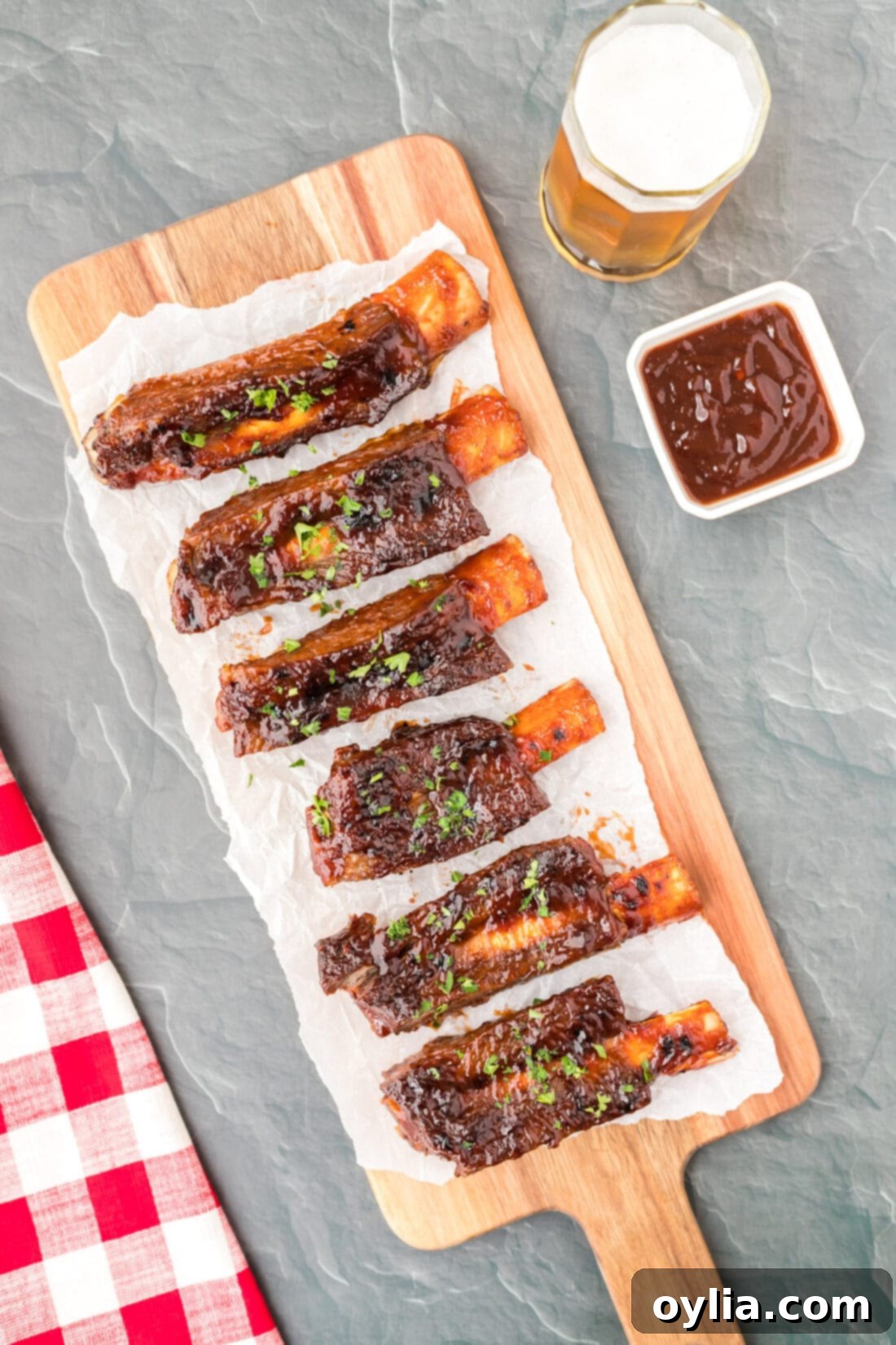 Tender Instant Pot Beef Ribs 5 Close-up of Instant Pot Beef Ribs on a cutting board, brushed with barbecue sauce and garnished with fresh herbs.