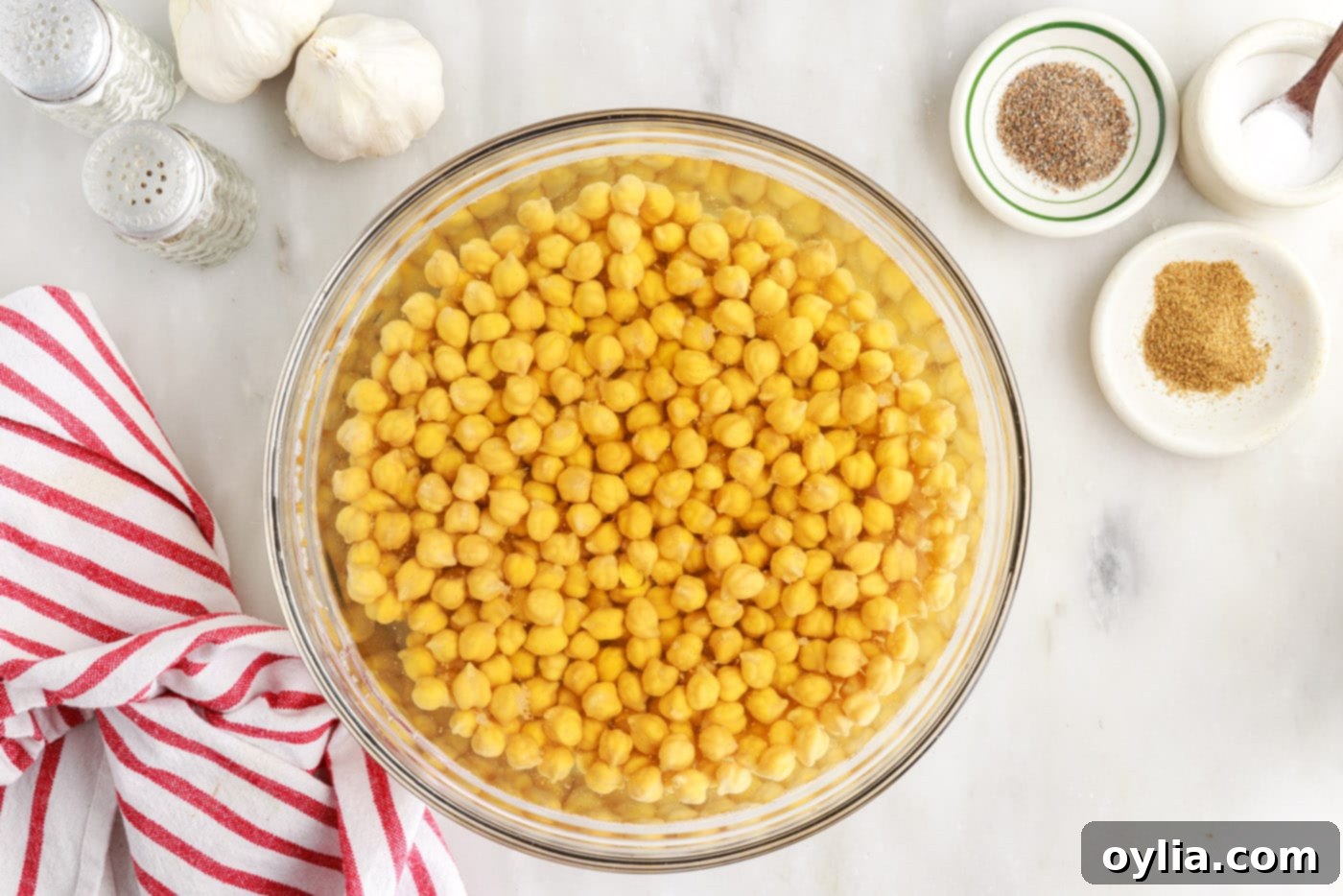 Dried garbanzo beans soaking in cold water in a large bowl, visibly expanding.