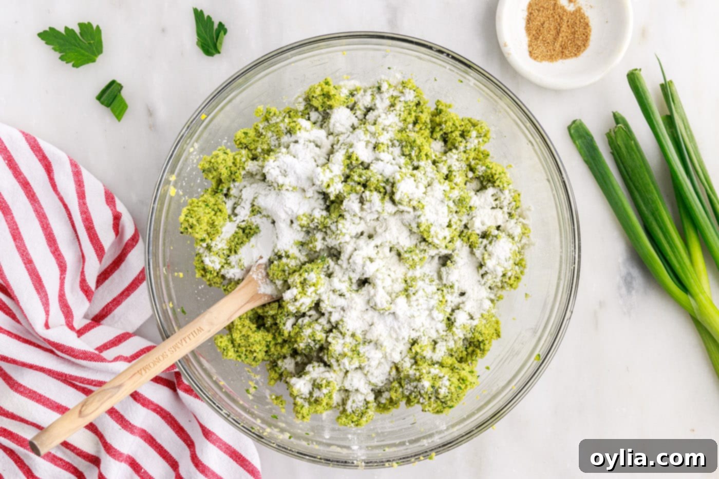 Flour and baking powder being sprinkled over the falafel mixture in a large bowl.