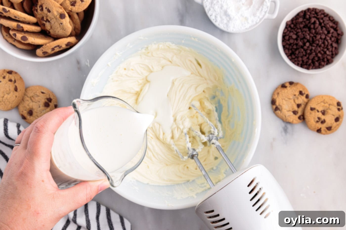 Pouring cold heavy cream into the cream cheese and sugar mixture, beating constantly to achieve a fluffy texture for the icebox cake filling