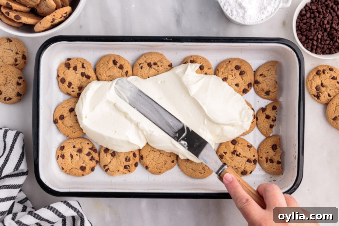Smoothly spreading the whipped cream cheese mixture over the first layer of chocolate chip cookies for the icebox cake