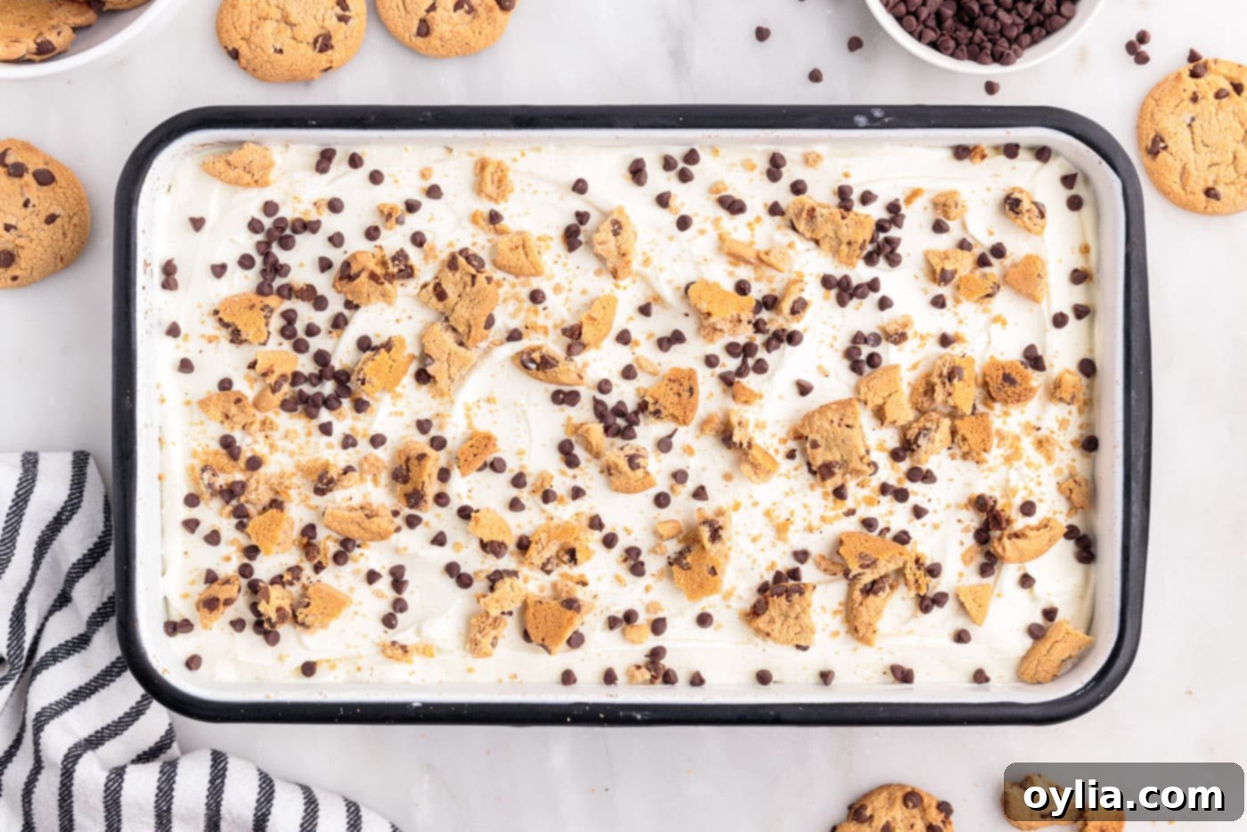 Overhead view of a fully layered chocolate chip cookie icebox cake, topped with cream and ready for garnishing and chilling