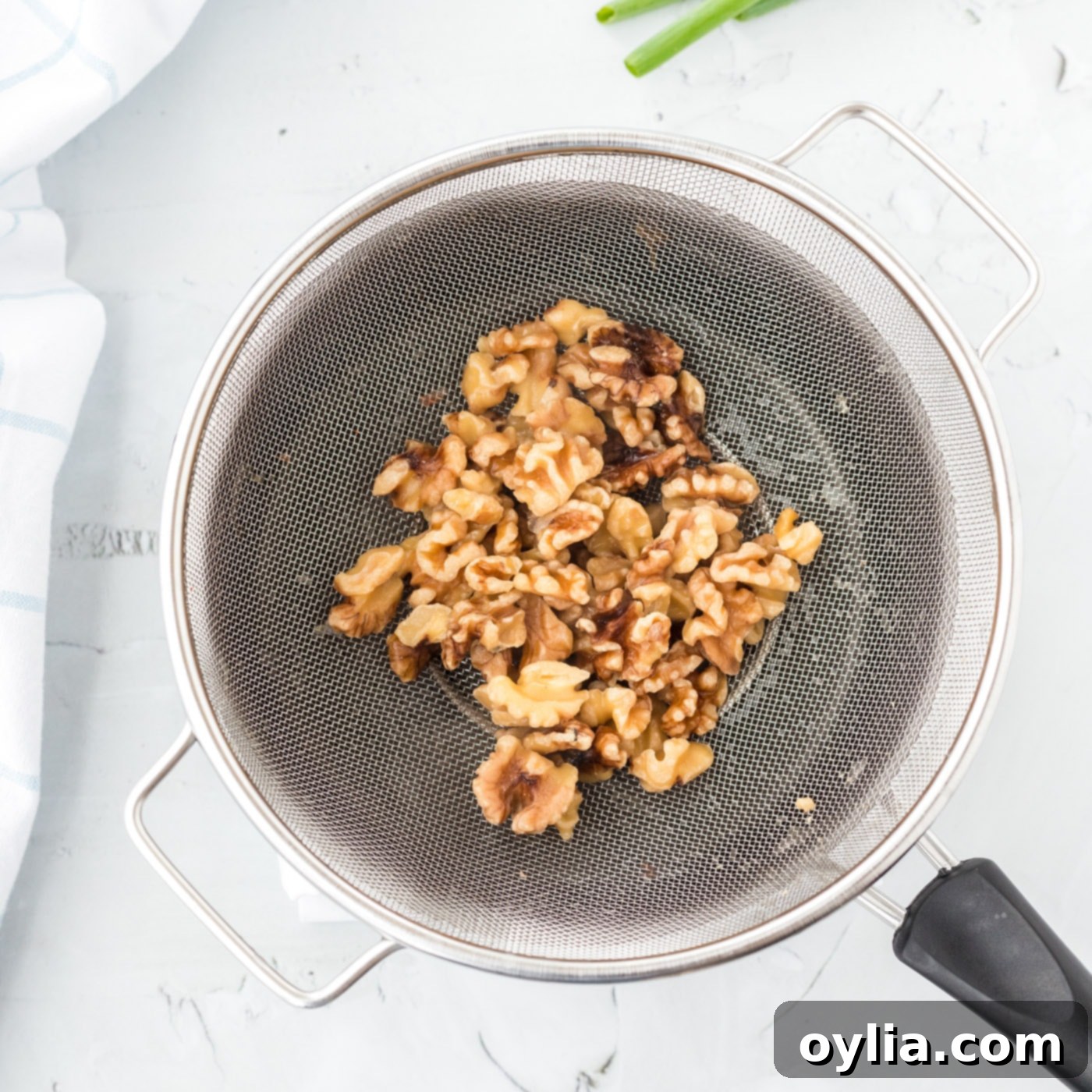 Candied walnuts draining in a colander after boiling, ready to be dried.