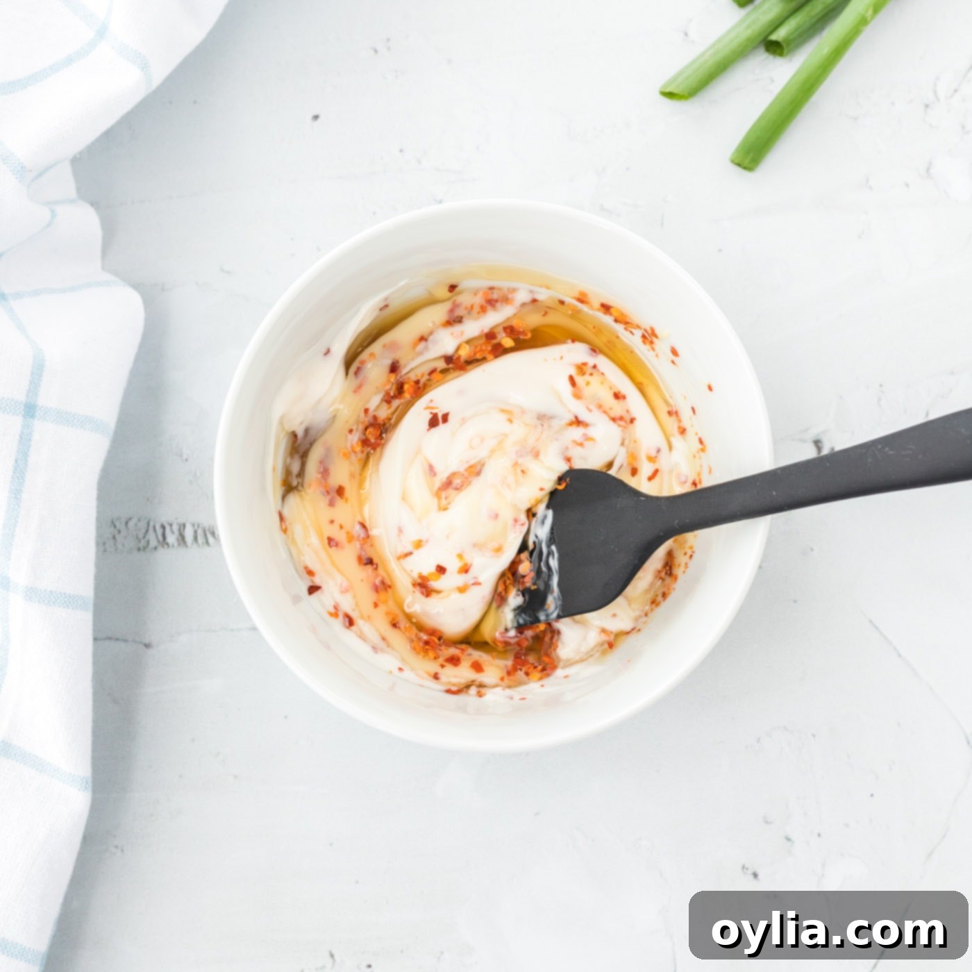 Spatula stirring the creamy honey walnut shrimp sauce in a bowl.