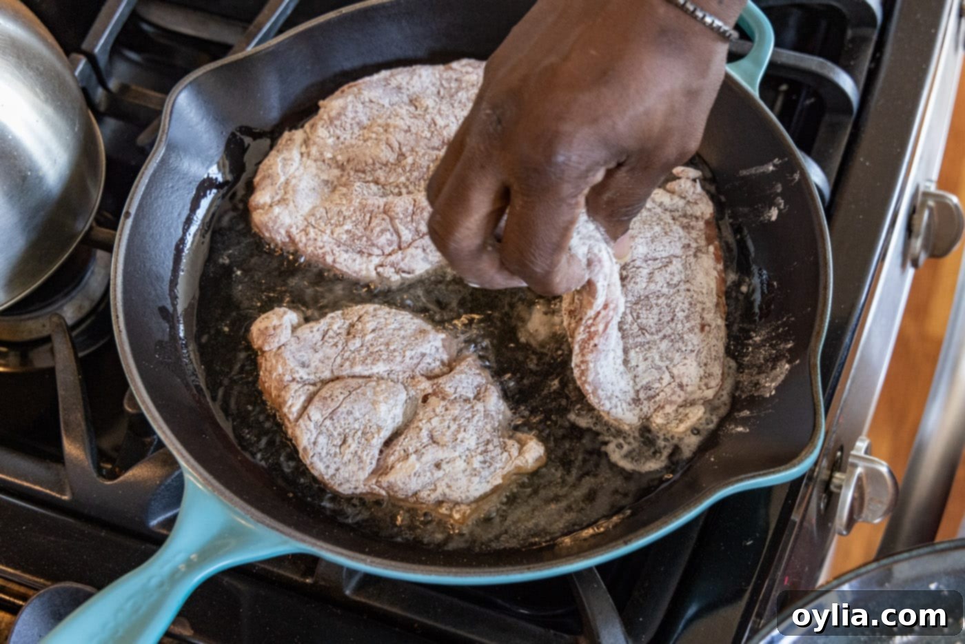 adding veal cutlets to a hot skillet with olive oil