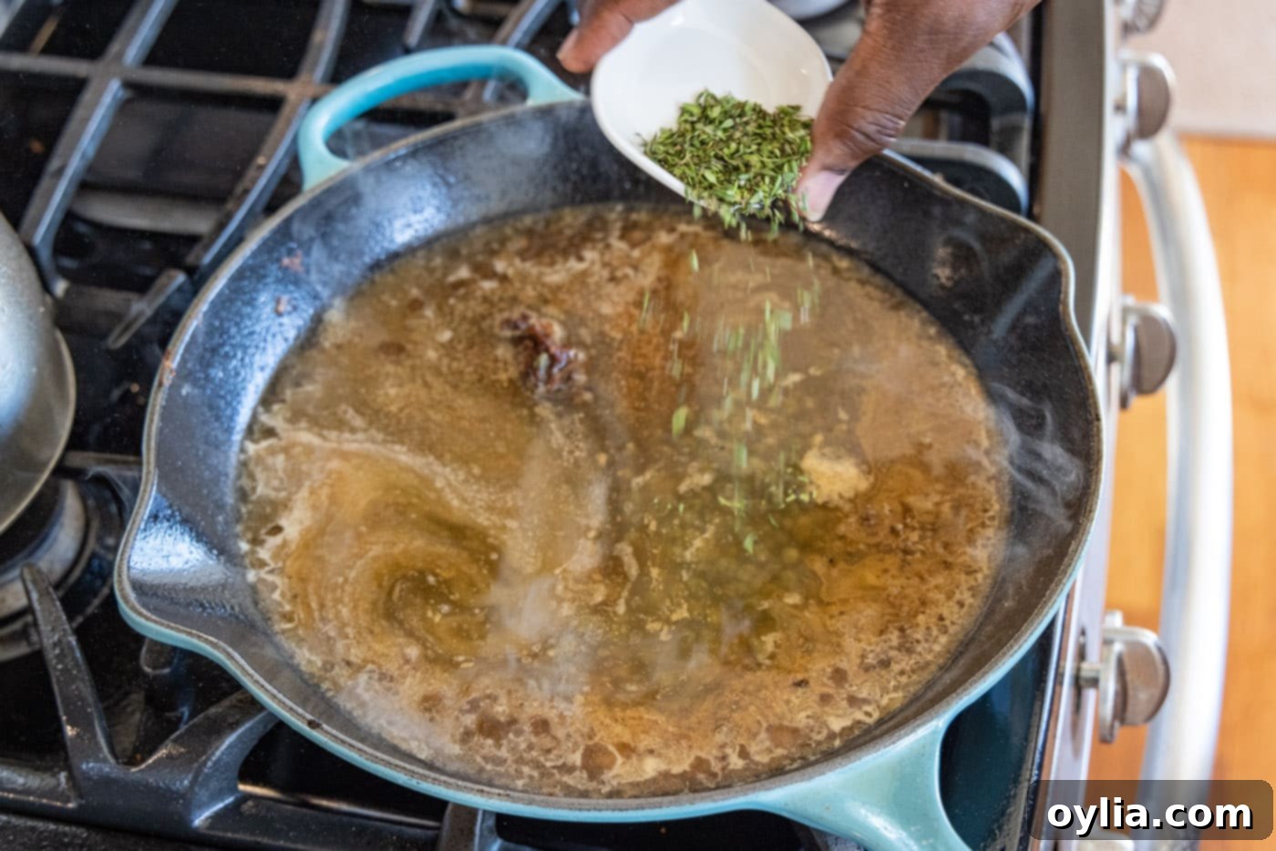 sprinkling fresh thyme into veal piccata sauce in a skillet
