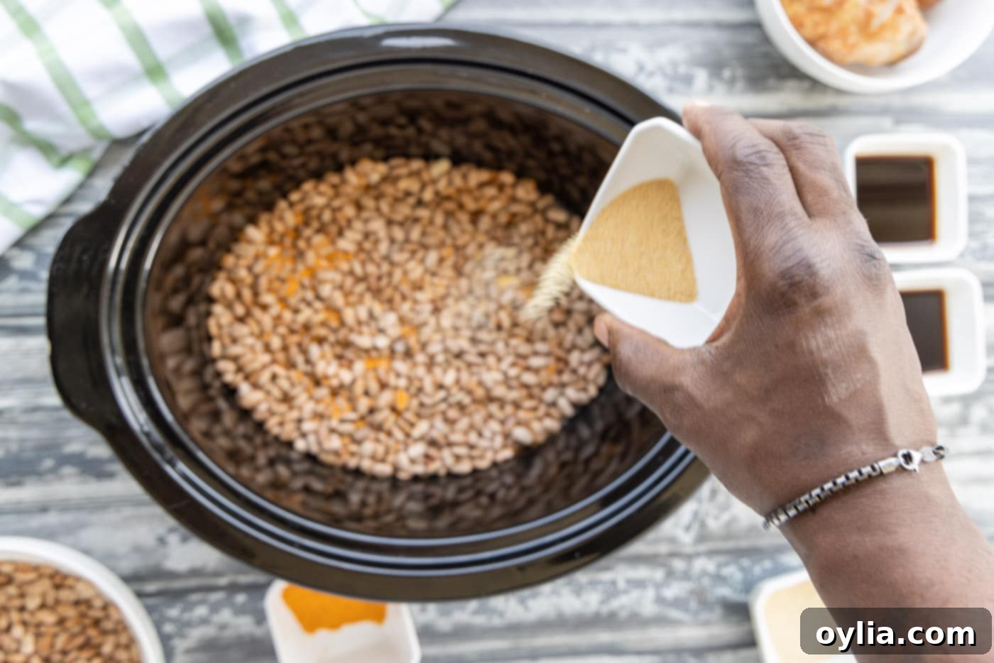 Seasoning being sprinkled over pinto beans in a slow cooker