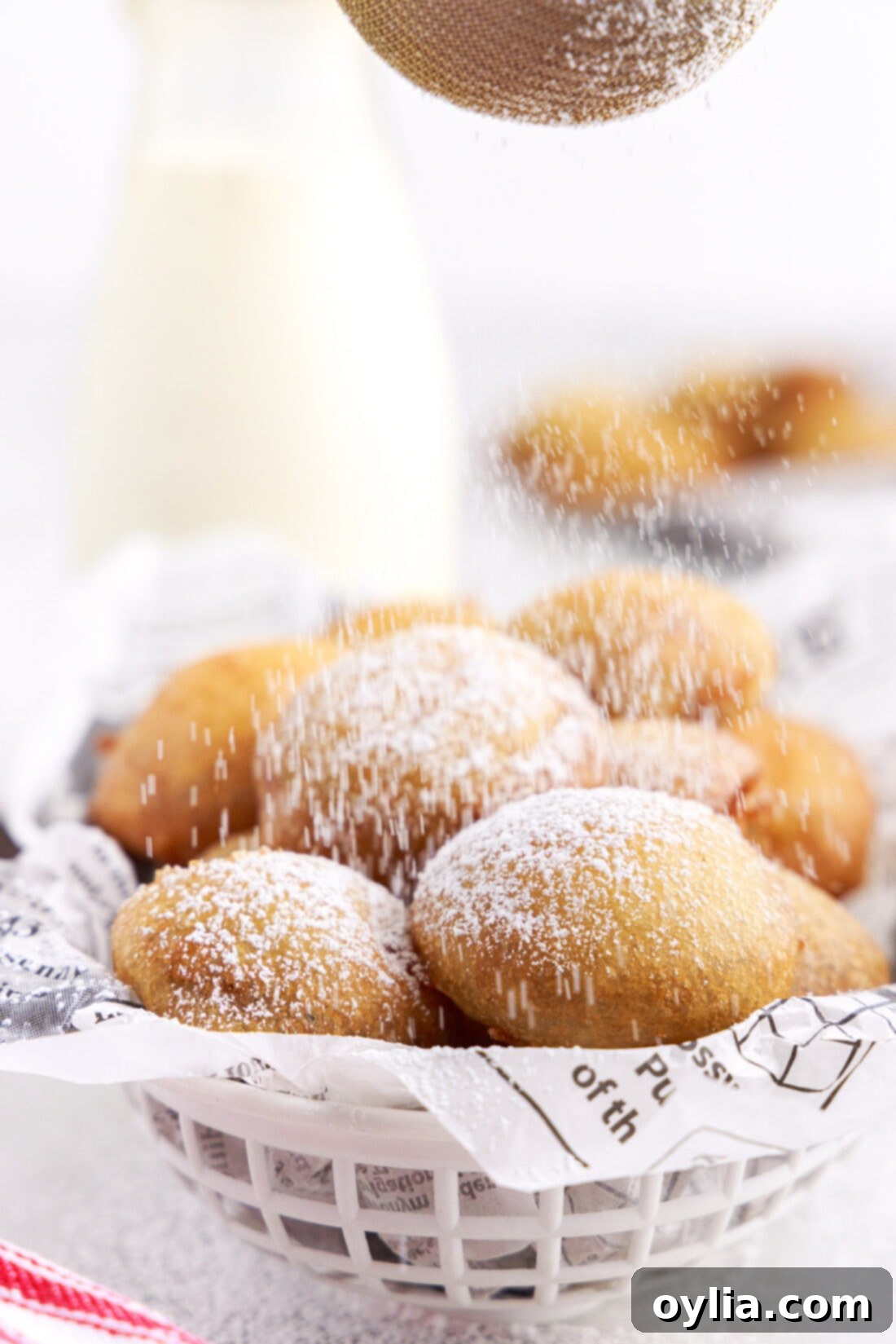 A person dusting freshly fried Oreos with powdered sugar, highlighting the final touch of this sweet treat.