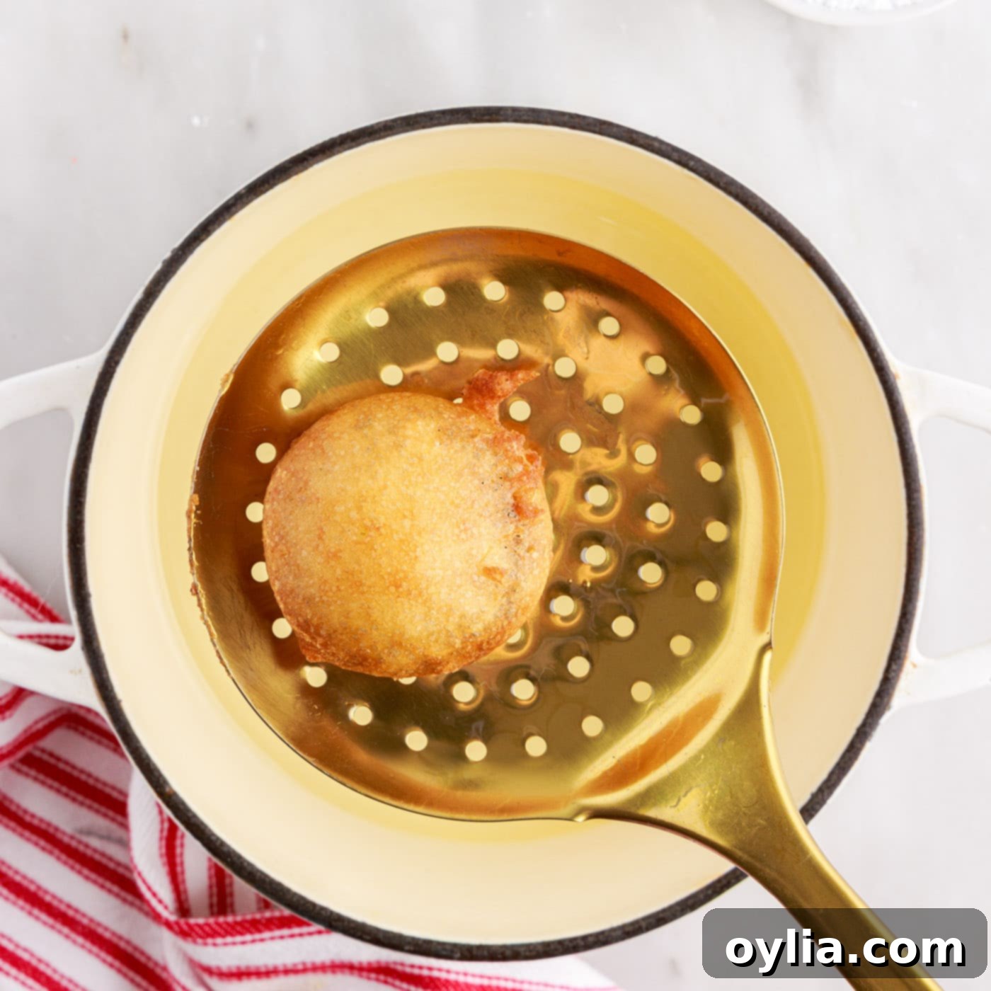 A deep fried Oreo being lifted from the hot oil with a slotted spoon, golden brown and perfectly cooked.