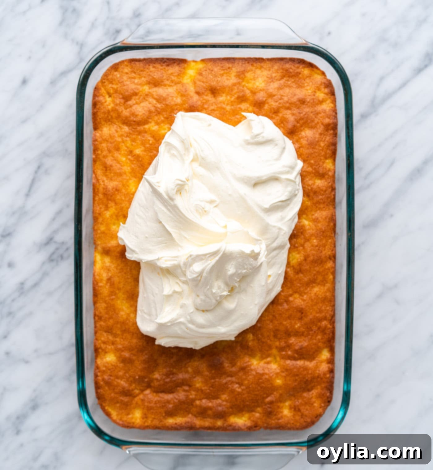 Spreading fluffy pineapple frosting evenly over the cooled yellow cake