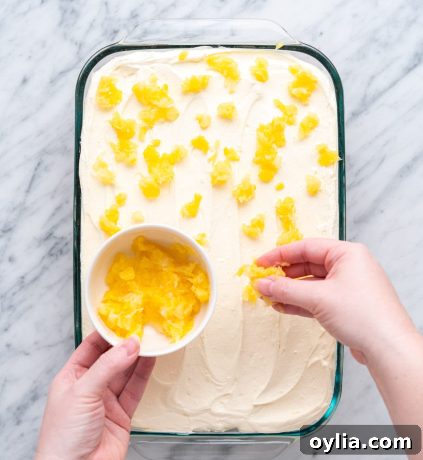 Sprinkling crushed pineapple on top of the frosted Pineapple Sunshine Cake