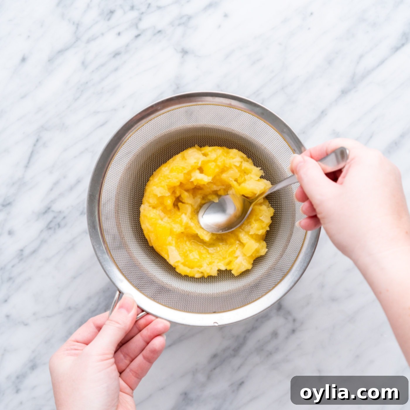 Straining crushed pineapple to separate juice for frosting and fruit for topping
